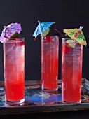 Three Singapore Slings with cocktail umbrellas on a tray