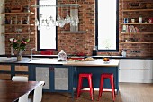 Red metal stools at island counter with ample storage space; kitchen counter against brick wall