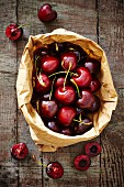 Fresh Spanish cherries in a brown paper bag on a wooden board