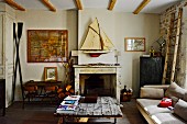 Rustikaler Couchtisch mit Platte aus Holzbrettern, im Hintergrund offener Kamin, darüber Modell Segelboot an Wand, in schlichtem Wohnzimmer