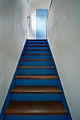 Blue-painted wooden staircase with plain wooden treads leading up between white walls; Mediterranean ambiance