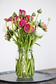 Bouquet of ranunculus in jar of water on tray