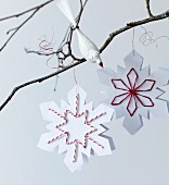 Paper snowflakes with embroidered details and bird ornament on bare branch