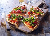 Pizza bread with tomatoes and rocket, sliced on a wooden board