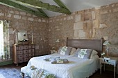 Stone walls, green-painted roof beams, antique chest of drawers and quilted bed cover in Mediterranean bedroom