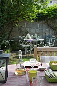Blick vom gedeckten Tisch in einen Garten mit verschnörkelten Gartenmöbeln aus Metall