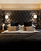 Masculine bed with black upholstered headboard, sconce lamps and dark scatter cushions