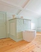 Modern toilet mounted on custom, half-height cabinet covered in pastel-green mosaic tiles