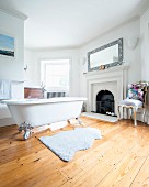 Free-standing bathtub with silver-gilt claw feet on wooden floor in spacious bathroom with open fireplace