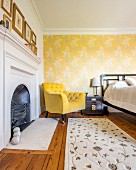 Fireplace, yellow armchair and wallpaper with floral pattern on yellow background in bedroom