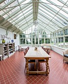 Long wooden table with turned legs in large conservatory with terracotta floor