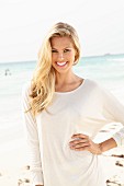 A young blonde woman on a beach wearing a long, white shirt