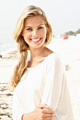 A young blonde woman on a beach wearing a long, white shirt