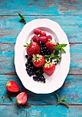 Fresh berries with mint leaves on a plate (seen from above)