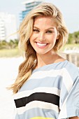 A young blonde woman on a beach wearing a striped summer blouse