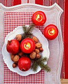 Fir twigs, nuts, pomegranates and apple-shaped candles on plate