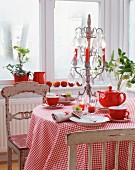 Rot-weiss gedeckter Kaffeetisch mit karierter Tischdecke, Kerzenleuchter und alten Stühlen