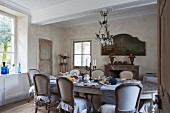 Long, oval dining table and antique upholstered chair in rustic yet stylish dining room
