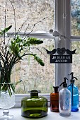 Vase of flowers, vintage glass bottles and soda siphon bottles on sill of lattice window