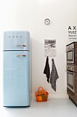 Pale blue retro fridge in modern kitchen with orange plastic basket on floor