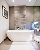 Modern, free-standing bathtub against stone wall with illuminated niche to one side
