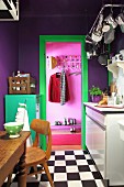 Violette Wände, grüner Metallschrank und Türrahmen in kleiner Küche mit Schachbrettmusterboden, Blick in pinkfarbene Diele