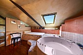 Modern, oval bathtub with massage jets in modern bathroom with sloping ceiling in Italian shades of terracotta