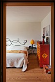 Blick in Schlafzimmer mit kunsthandwerklichem Bettkopfteil, Nachttisch und orangeroter folkloristischer Kommode - in einem Fertighaus