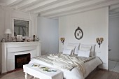 White, rustic bedroom with open fireplace and ensuite bathroom behind partition