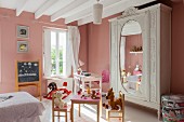 Pink walls, play table and antique wardrobe in vintage-style child's bedroom