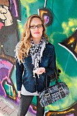 Junge Frau in Jeansjacke und Halstuch vor Graffiti-Wand