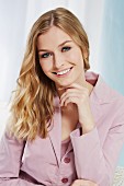 A portrait of a blonde woman wearing a dusky pink blouse and a blazer