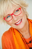 An older woman wearing an orange jumper and scarf and a pair of red glasses