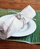 Leinenserviette mit Steindekoration auf weißem Teller, darunter ein Bananenblatt als Tischset