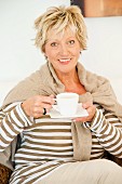 An older woman wearing light clothing sitting down with a cup of coffee