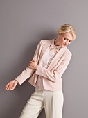 A woman wearing a pink blouse and a blazer with a pair of white trousers