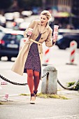 A young woman wearing a polka-dot dress and a woollen coat balancing three cups of coffee