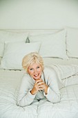 Ältere Frau in weißem Pyjama und Strickjacke liegt auf Bett