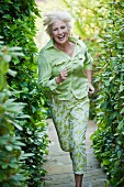 An older woman wearing a light green blouse and green-and-white trousers running in a garden