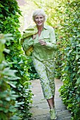 An older woman wearing a light green blouse and green-and-white trousers in a garden