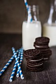 Gestapelte Oreo Cookies, gestreifte Strohhalme und zwei Flaschen Milch