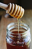 Honey trickling from a honey dipper into a jar