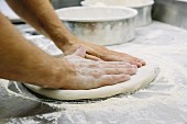 A pizza baker flattening dough