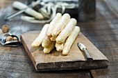 Fresh white asparagus on a chopping board next to a nutmeg grater with nutmegs