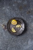 A lemon half and a halved lemon slice on a metal plate (seen from above)
