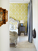 Baroque bed frame and bedside table in front of yellow wallpapered wall