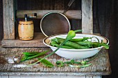 Young pea pods in a bowl on an old wooden table with a spilt salt shaker