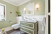 A country house chest of drawers with a marble top used as a wash basin in a pale green painted bathroom