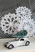 Toy car with Christmas tree on roof in front of paper snowflakes