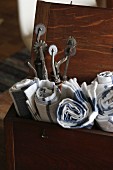 Gerollte Küchenhandtücher und Vintage Perforierwerkzeuge in alter Holzkiste mit offenem Deckel